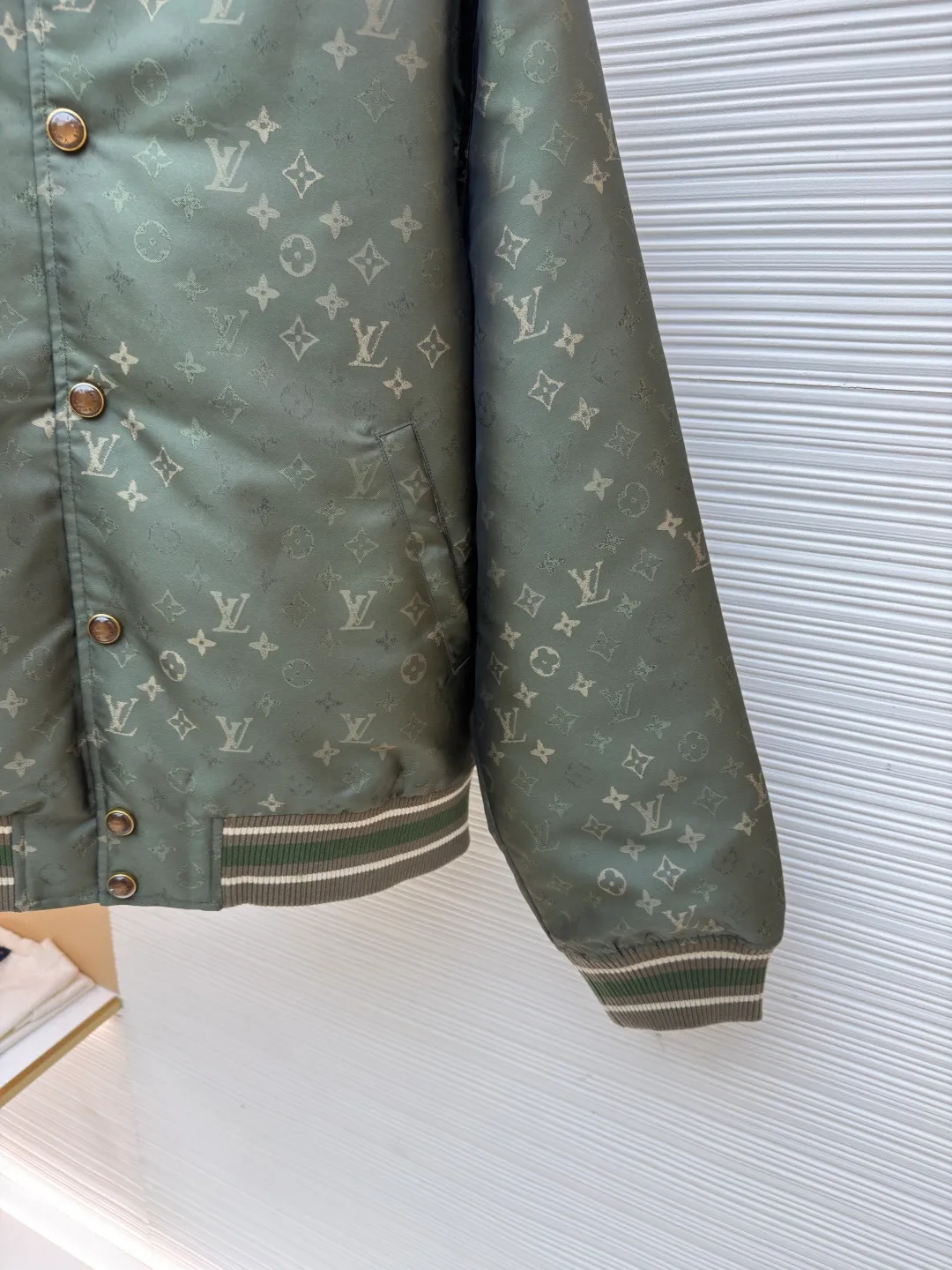 LOUIS VUITTON striped trim jacquard long-sleeved bomber jacket ●Original version: purchased and developed by 29237 ●Item number: 1682087-C05 ●Fabric: nylon fabric ●Technology: jacquard production ●Color: green ●Version: fitted version ●Weight: about 800 grams ●Size: S-M-L-XL ●Description: This Louis Vuitton baseball jacket is made of high-density jacquard satin fabric. The base is a polyester fiber blended material with a military green matte texture. The classic Monogram presbyopia pattern is woven into the fabric in the form of dark patterns of the same color through a special weaving process. The pattern texture is three-dimensional and presents a delicate illusion luster with the angle of light. High-precision jacquard weaving technology is used in the process to ensure the integrity and delicacy of the pattern. The body adopts a single-row metal snap closure design. The metal buckles are matte and distressed to echo the color of the body. The ribbed collar, cuffs and hem are made of two-color knitting technology. The elastic ribs have both stiffness and comfort, and are pre-shrunk to prevent deformation. The overall cut is a loose oversize version, and the splicing uses a combination of flat seams and hemming techniques. The interior is supplemented by smooth overlock sewing. Every stitch is even and fine, which fully reflects the brand's exquisite garment production technology and detail control. The overall wiring is straight and delicate, the fabric is comfortable and soft, and the color is consistent without color difference. It can be matched with the same style to create a fashionable look and control various occasions. Customized accessories, complete with three standards, same style for men and women!